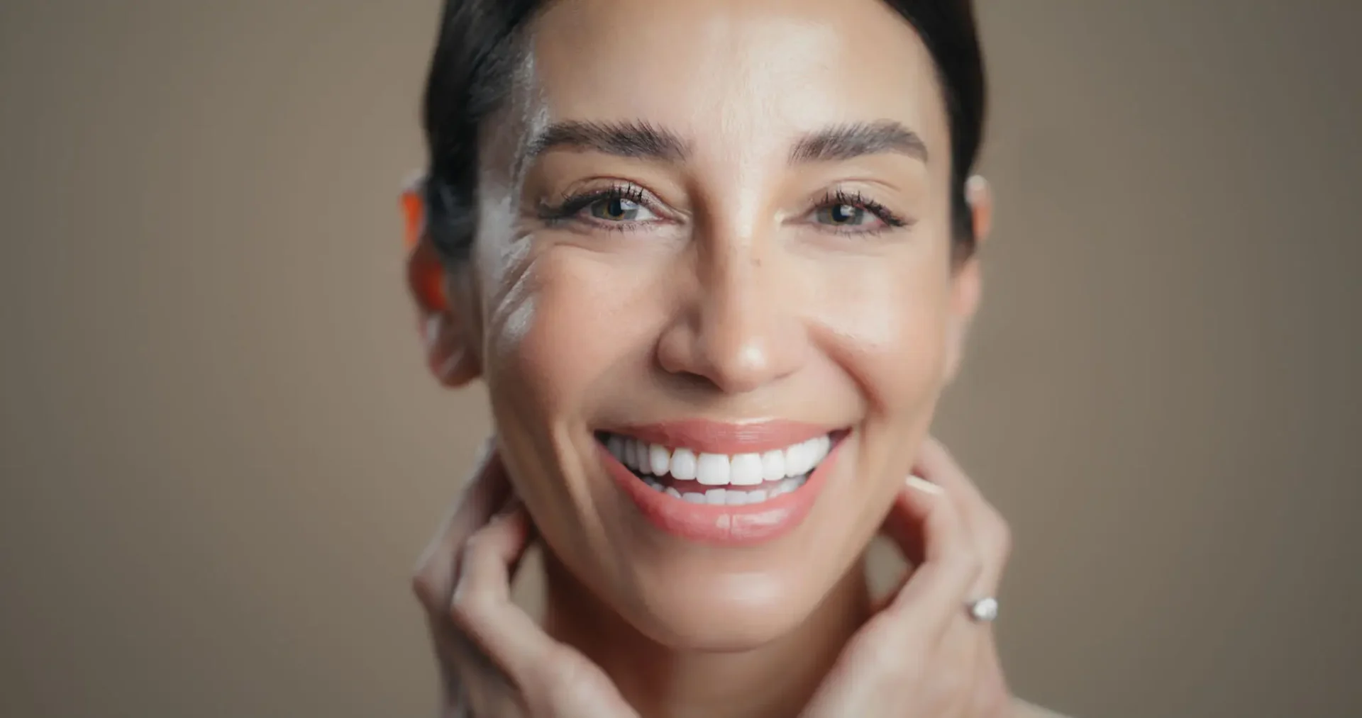 Close-up of a smiling woman with radiant skin and natural makeup.